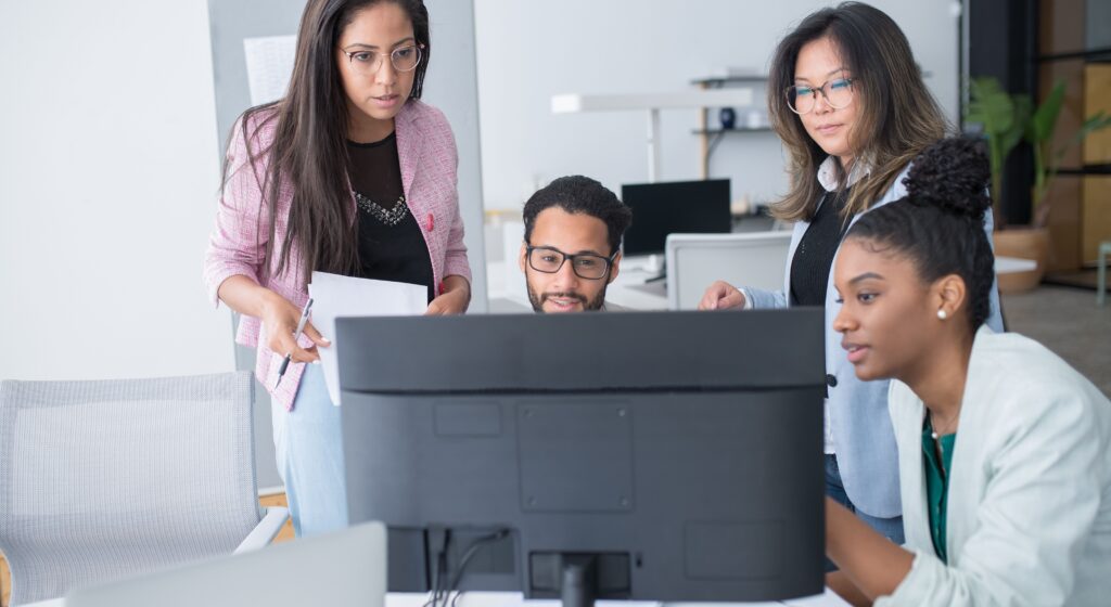 Equipo diverso de Recursos Humanos revisando conjuntamente un plan de formación en un monitor, ilustrando el uso de un software LMS centralizado en la oficina.