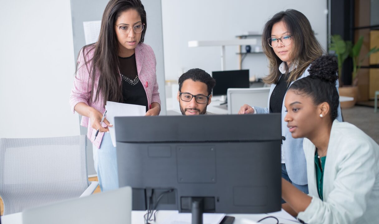 Equipo diverso de Recursos Humanos revisando conjuntamente un plan de formación en un monitor, ilustrando el uso de un software LMS centralizado en la oficina.