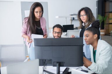 Equipo diverso de Recursos Humanos revisando conjuntamente un plan de formación en un monitor, ilustrando el uso de un software LMS centralizado en la oficina.
